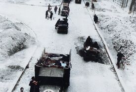 Photo prise en hauteur sur le pont Albert 1er, en haut à gauche rue Lille, à la droite l'ancien cinéma Palace avec le trottoir plein de gravats. Vu du pont un camion au premier plan et derrière une suite des jeeps et des badauds de chaque côté de la rue. 